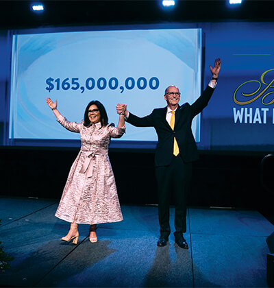 Leticia “Leti” Contreras (B.A. ’89), Trustee Emerita, and Thomas M. Mengler unveil the grand total raised during The Defining Moment Comprehensive Campaign — $165 million.