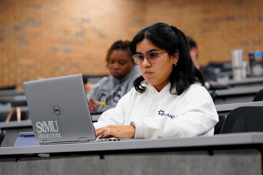 Student focused on laptop in classroom taking notes.