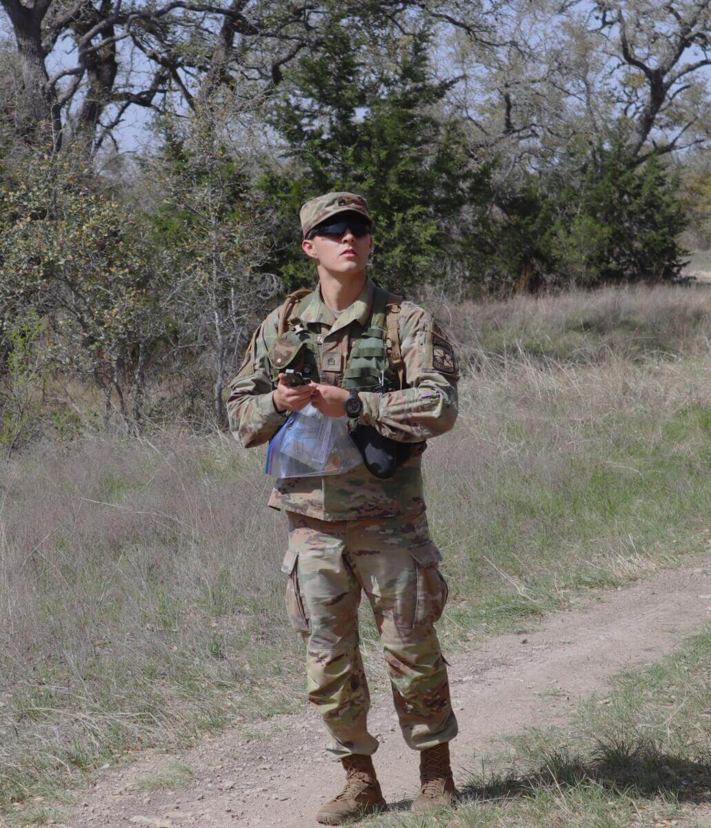 Male ROTC student holding compass navigates around the forest side.